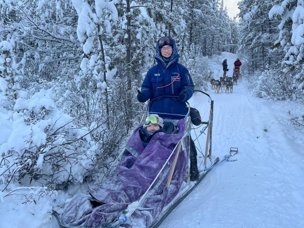 Person on a snowy path riding a sled pulled by huskies.