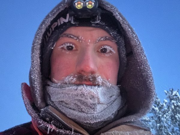 Person with frost-covered face wearing headlamp and winter gear.